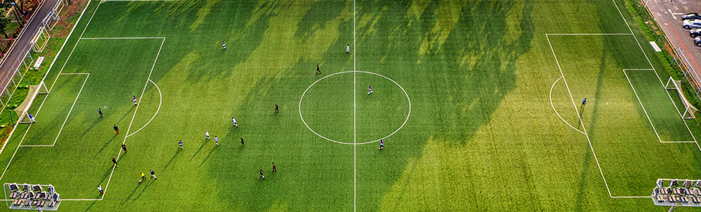 Drone shot of people on a green football pitch, playing football.