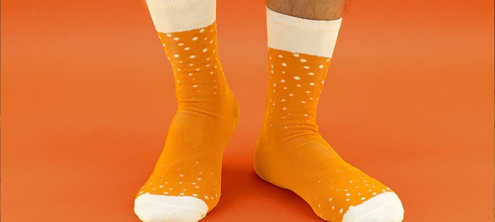 Close-up of a person wearing Luckies of London Beer socks standing on an orange background